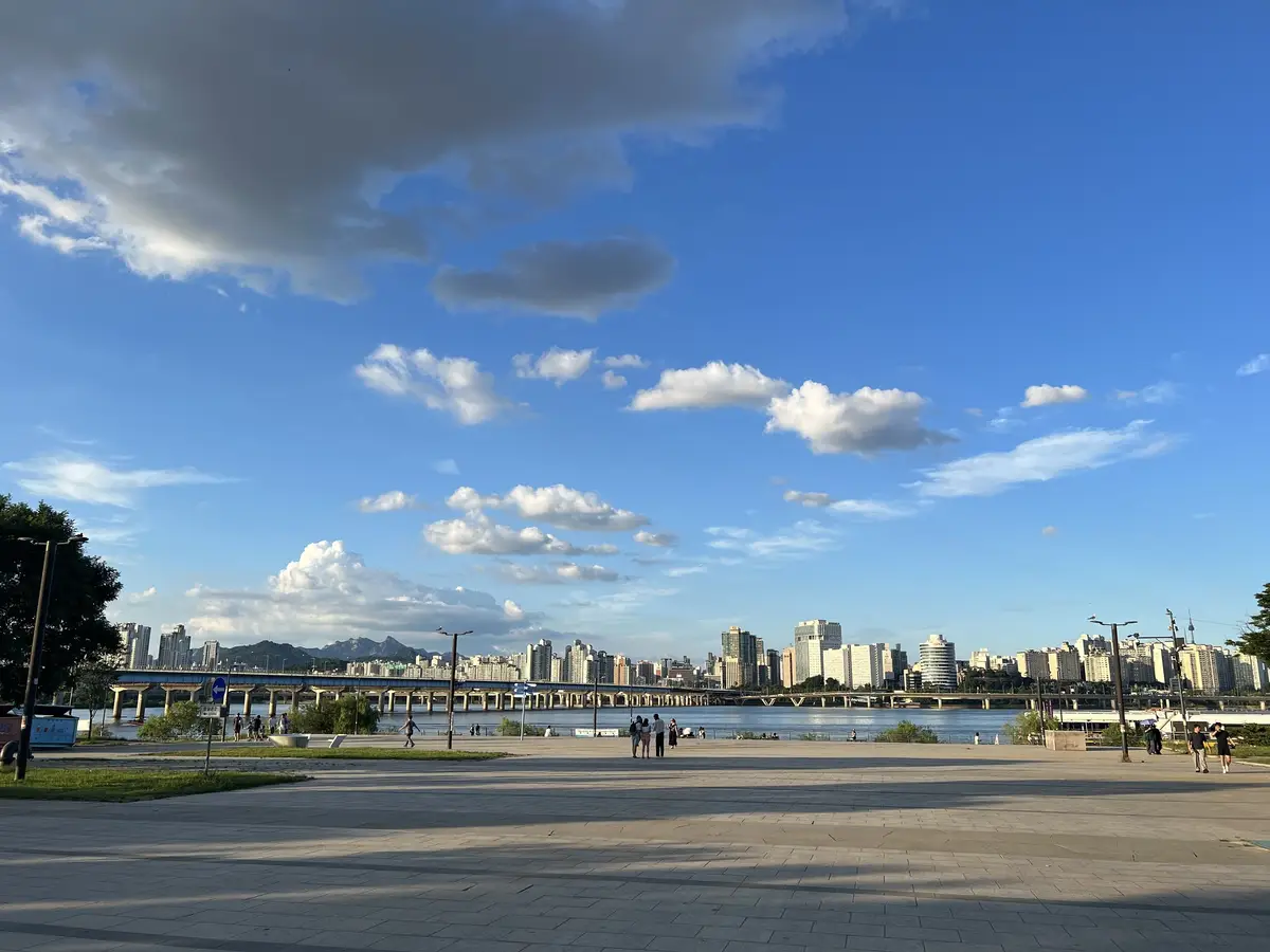 A wide riverside plaza in a Hangang park under a blue sky with scattered clouds
